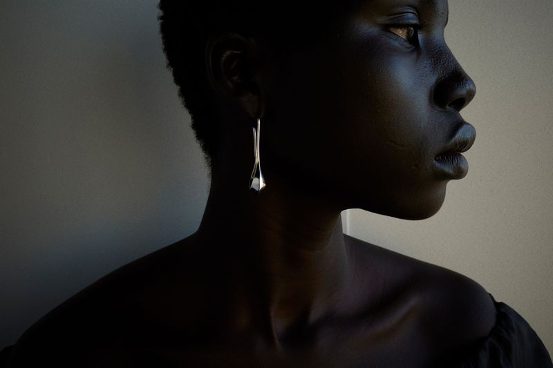 Profile portrait of a Black woman wearing a silver drop earring against a neutral background for Lemaire Lookbook S/S 25.