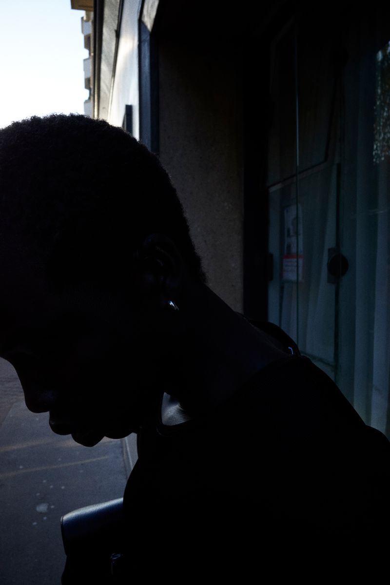 Silhouette of a dark-skinned person standing indoors near a window with visible natural light creating a high-contrast black image.