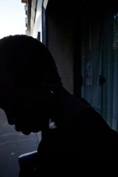 Close-up silhouette profile of a model with short dark hair against a building exterior backdrop.