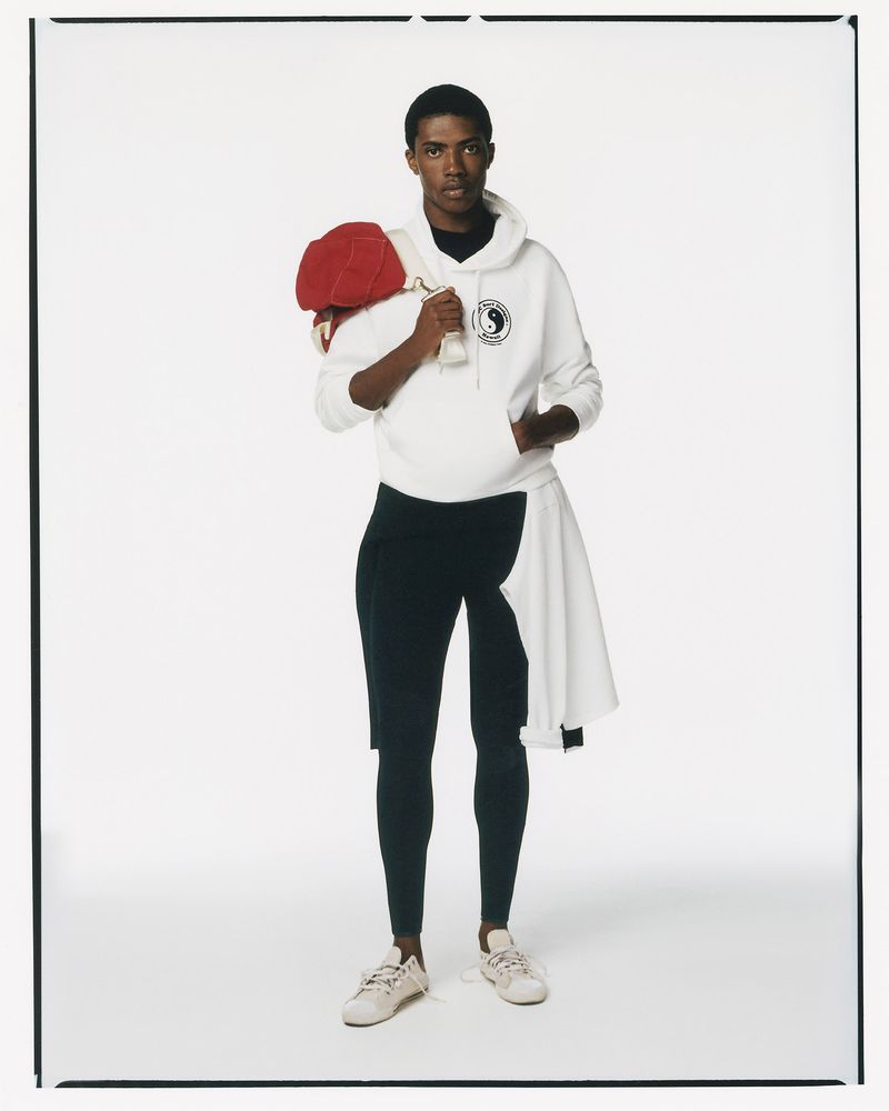 Athletic man in studio wearing sporty outfit and carrying a red cap, posing against a clean white backdrop in a full-length shot.