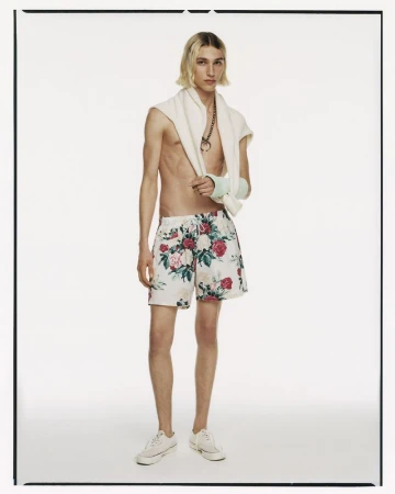 Male model wearing floral swim shorts and white canvas sneakers standing against a plain white background.