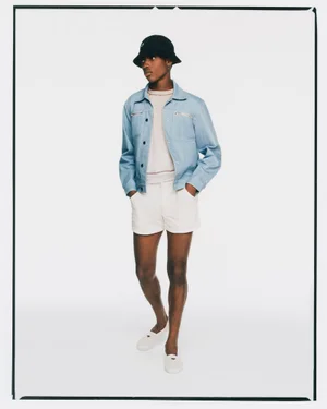 Model wearing a light blue jacket, white shorts, and black bucket hat against a white seamless background