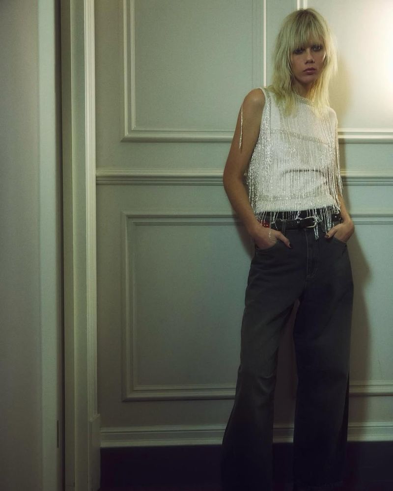 Model Marjan Jonkman wearing a fringe top and dark trousers indoors against a panelled wall