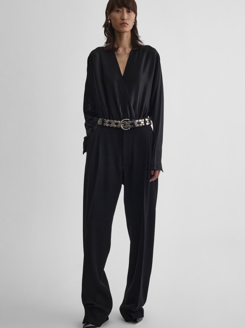 Full-length studio shot of a stylish Asian woman in a black jumpsuit with a metallic belt on a white background.