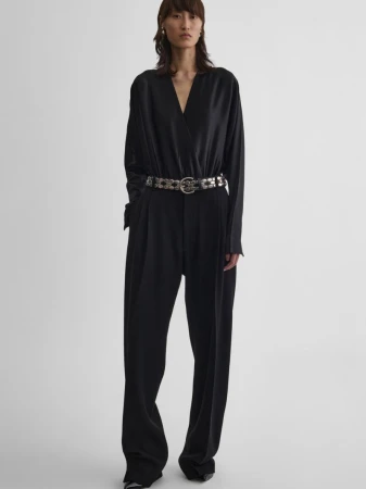 Full-length studio shot of a stylish Asian woman in a black jumpsuit with a metallic belt on a white background.
