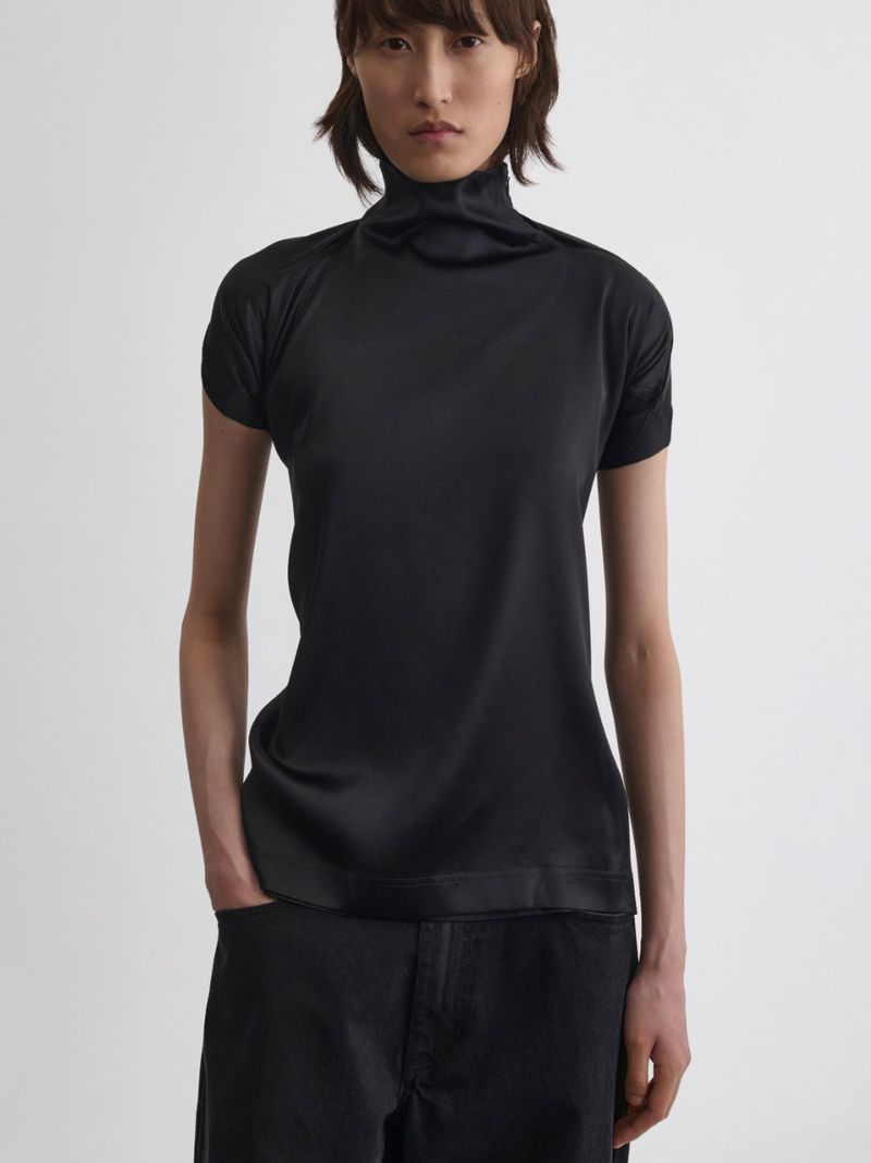 Model wearing a black turtleneck top and dark trousers against a plain white background for Phoebe Philo.