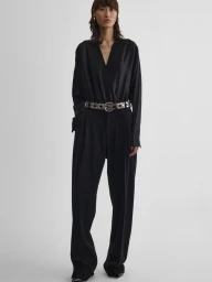 Model in black wrap top and trousers with embellished belt against white background