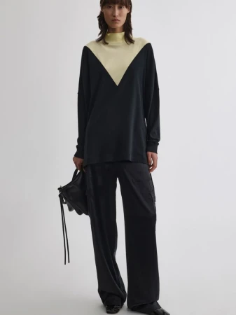Model wearing a black top with pale yellow v-paneled neckline and black trousers holding a black handbag