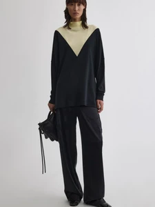 Model wearing a black top with pale yellow v-paneled neckline and black trousers holding a black handbag