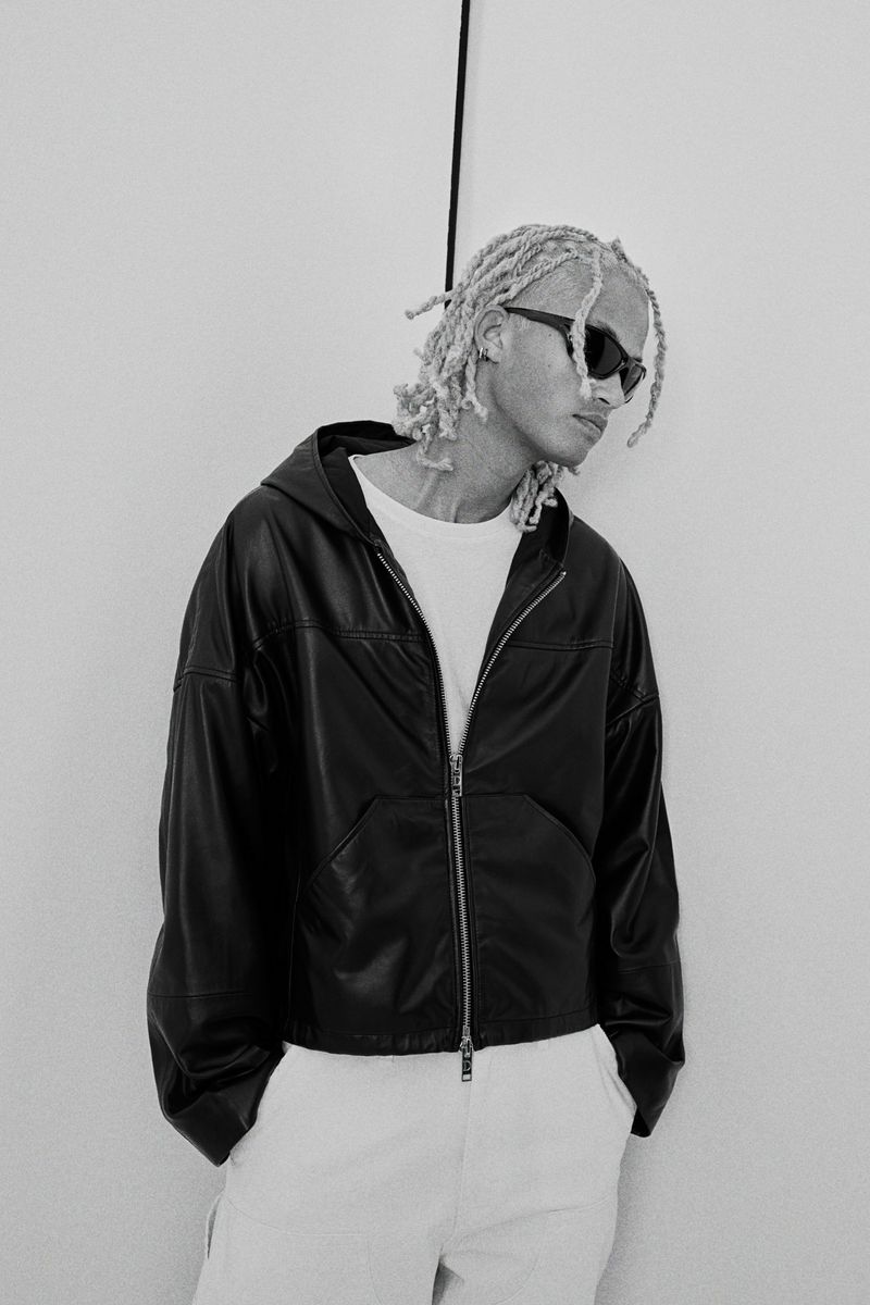 Model wearing black leather jacket and sunglasses standing against a plain white background for H&M.