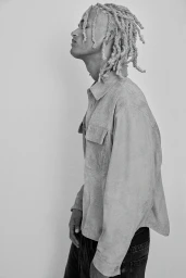 Profile portrait of a young man with blonde dreadlocks wearing a light suede shirt against a plain light background