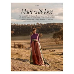 Woman in purple turtleneck and patterned wool blanket skirt standing in an open grassy field with rolling hills