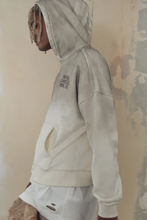 Fashion shot of a slender person wearing a gray and white hoodie with text, paired with white shorts and tan, distressed pants. 