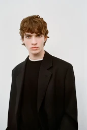 Portrait of a male model wearing a black blazer and crewneck sweater against a plain white studio background.