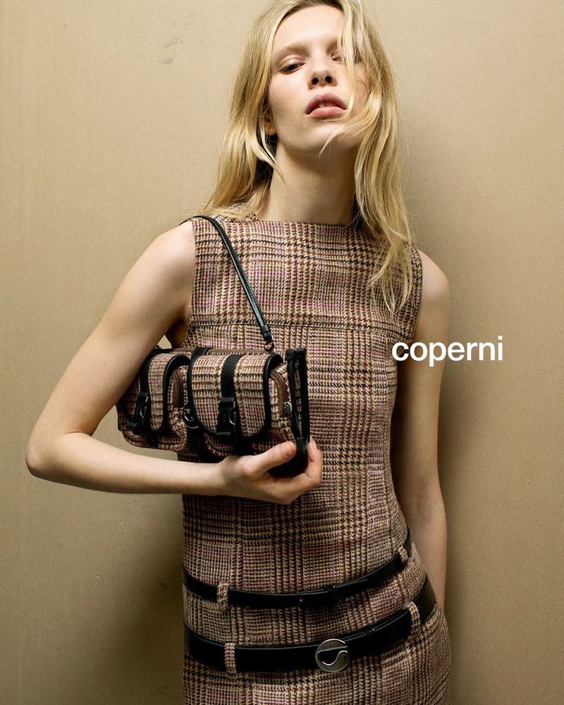 Fashion editorial shot of a blonde woman in a plaid dress, holding a structured bag. Coperni logo is visible. Studio shot on neutral backdrop.