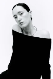 Model wearing an off-the-shoulder black top and silver collar necklace against a clean white background