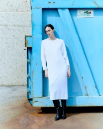 Model Helena Severin in a white dress and black boots leaning against a large blue metal container