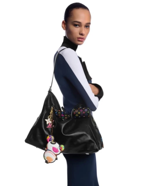 Woman wearing navy and white color block top, purse on shoulder with charm. Fashion editorial style, studio lighting, full shot.