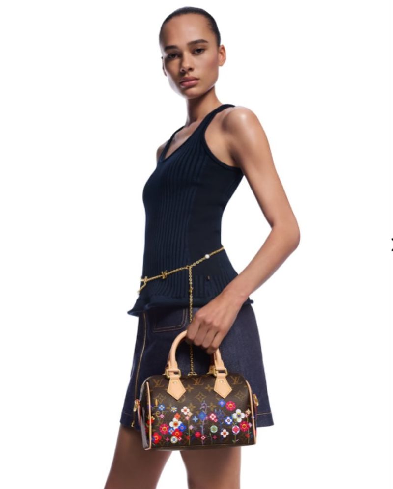 Model wearing a dark blue ribbed tank top and denim skirt holding a monogram floral handbag against a white background