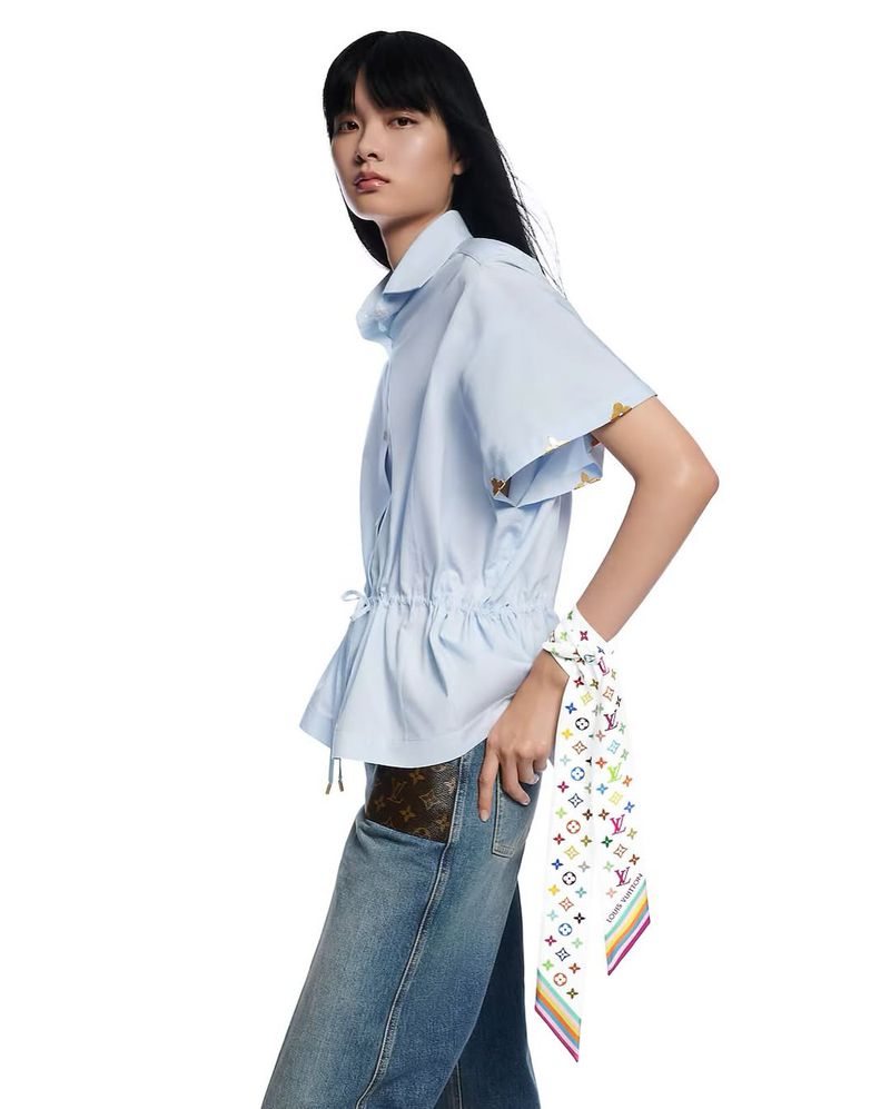 Fashionable Asian woman in a light blue top and jeans, posing in a studio. Features a colorful scarf, and a Louis Vuitton accent.