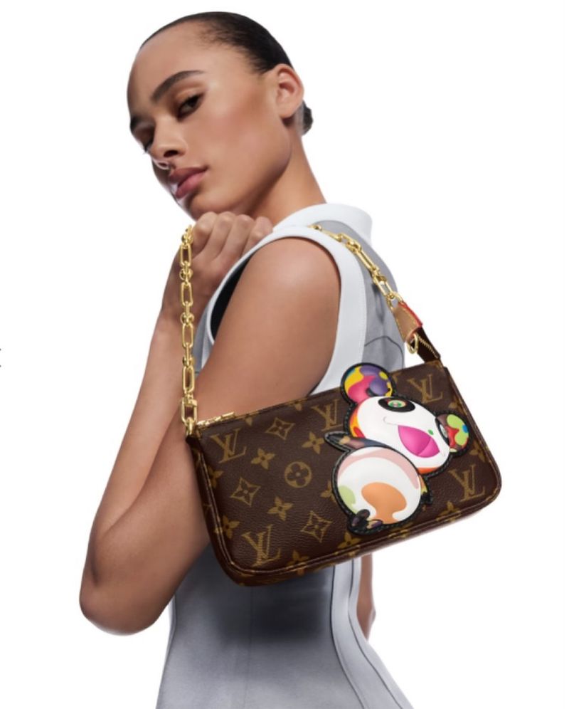 Adult woman poses in a studio holding a brown Louis Vuitton handbag with a gold chain and an animated character graphic on it.