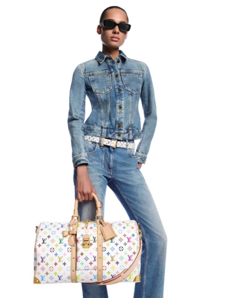 A light-skinned model poses in a denim jacket and jeans, holding a Louis Vuitton bag with a multicolored monogram pattern against a white backdrop.
