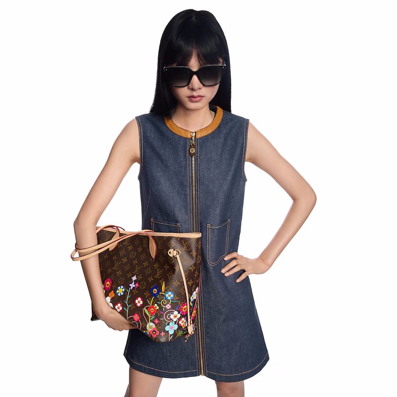 Woman in a denim dress holds a brown Louis Vuitton handbag with floral embroidery against a white background in a studio setting.