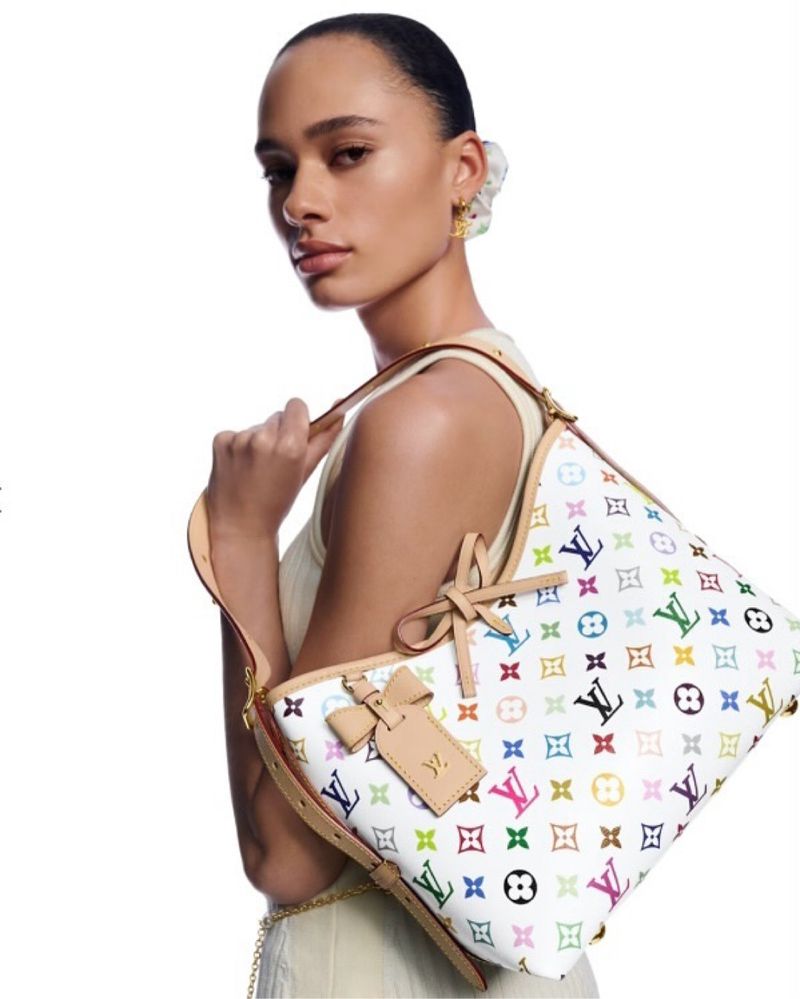 Model wearing light top holding a white multicolour monogram shoulder bag against a white background