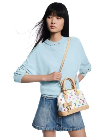 Model with long black hair wearing a light blue sweater and denim mini skirt holding a multicoloured monogram handbag
