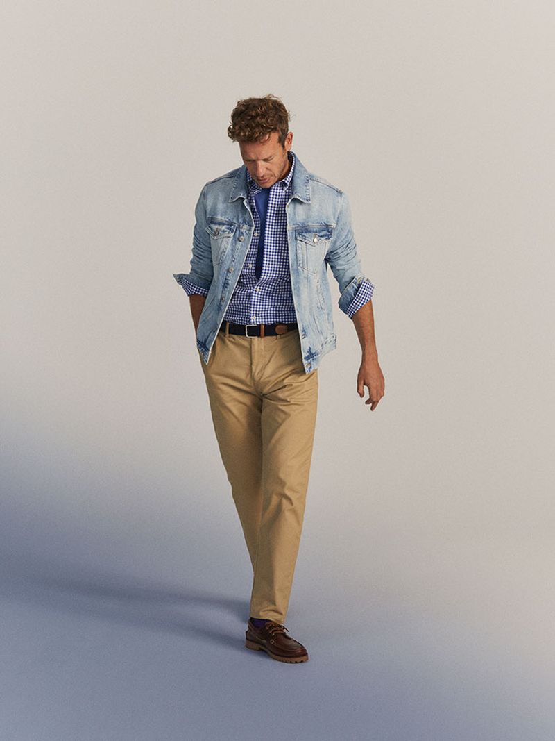 Adult male wearing a denim jacket and khaki pants in a full shot pose on a light grey background, fashion portrait showcasing classic apparel.