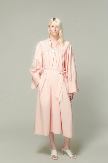 Full-length shot of a light-skinned young adult female model with platinum blonde hair wearing a pink dress and white heeled sandals.