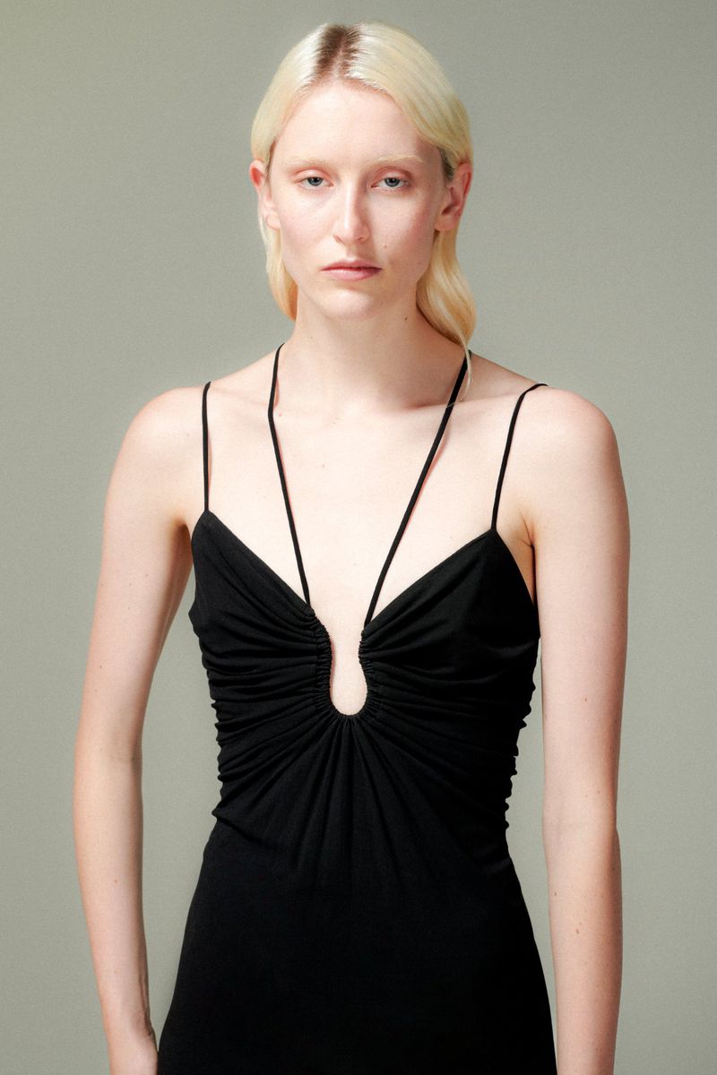 Close-up shot of a young woman with fair skin and blonde hair wearing a black sleeveless dress posing in a photo studio.