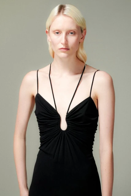 Close-up shot of a young woman with fair skin and blonde hair wearing a black sleeveless dress posing in a photo studio.
