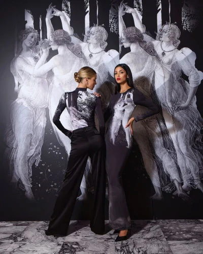 Two models posing in printed apparel against a large black and white classical allegorical mural backdrop.