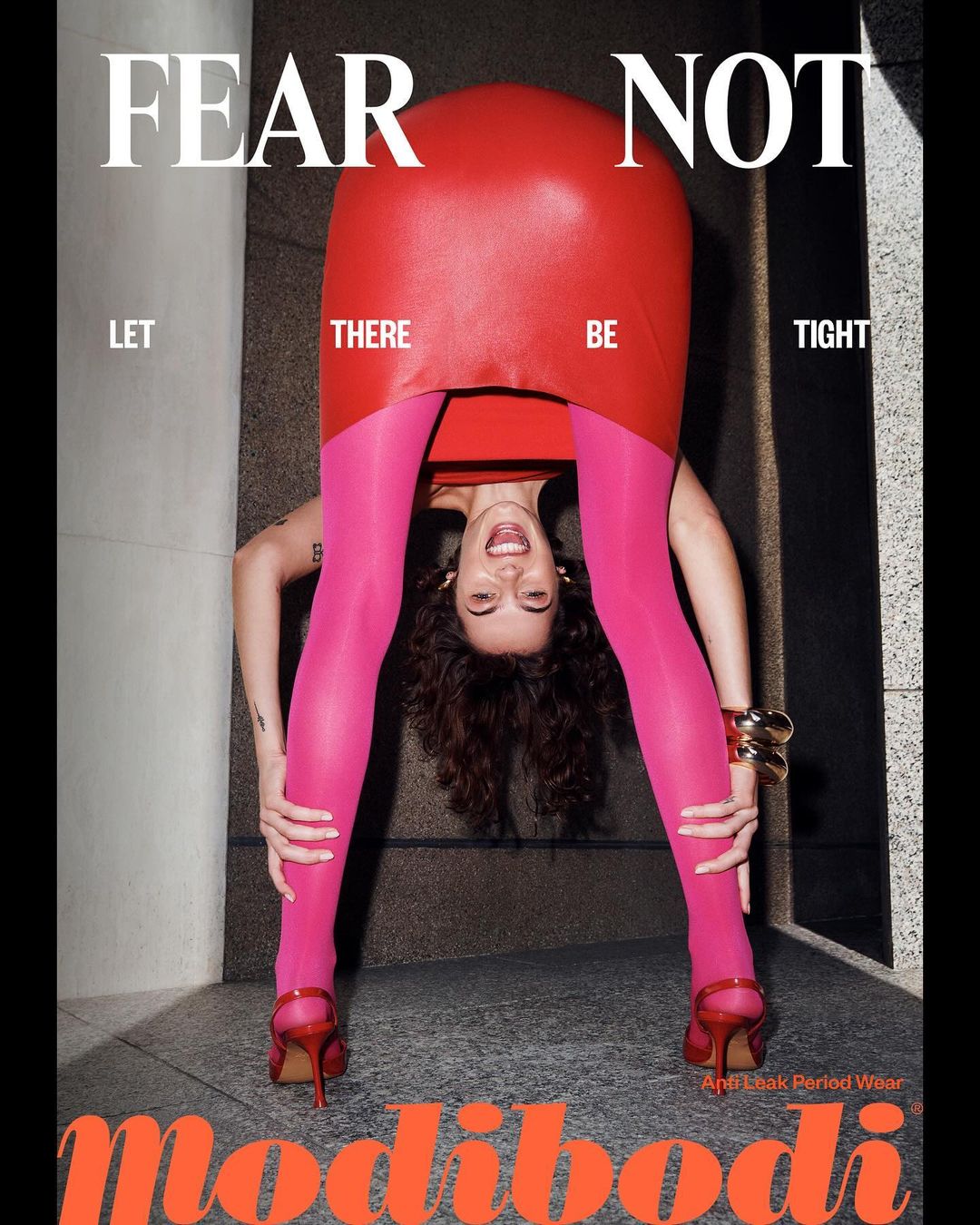 Modibodi campaign image featuring a woman in a red dress and pink leggings, bent over with her head visible between her legs.