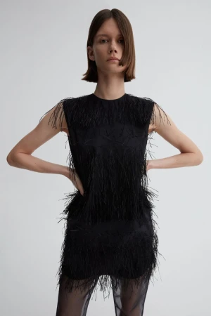 Model wearing a black fringed sleeveless top against a pale grey background for Gabriele Colangelo Resort 2025.
