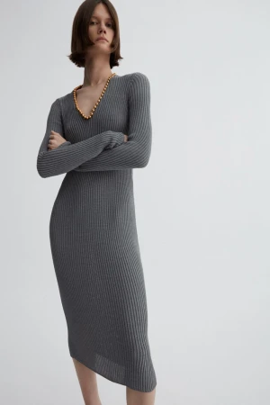 Model wearing a grey ribbed knit midi dress with arms crossed and gold necklace against a plain background