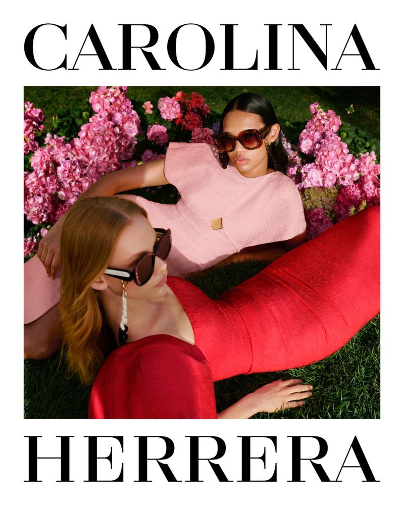 Two female models wearing sunglasses lying on a grass lawn surrounded by pink flowers for Carolina Herrera SS24