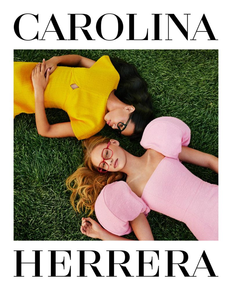 Two female models lying on lush green grass wearing a yellow dress and a pink puff-sleeve dress