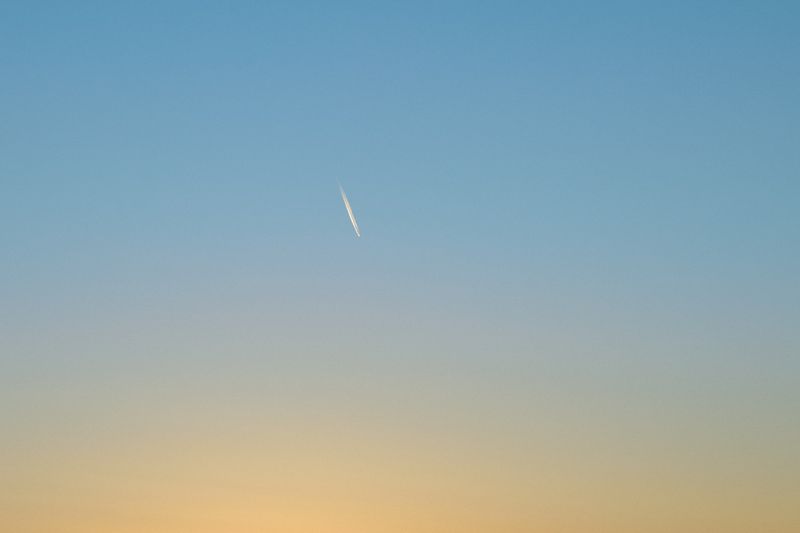 Sky with airplane contrail. Bright daytime scene with wispy vapor trail against a gradient of blue and yellow sky.