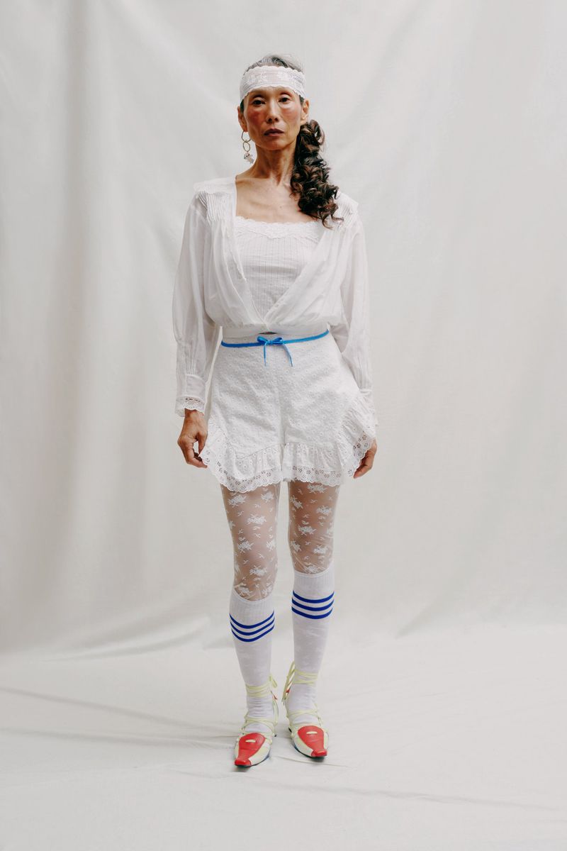 An Asian adult female fashion model in white lace shorts, top and white headband posing in studio, wearing sporty red and white shoes.
