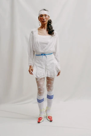 An Asian adult female fashion model in white lace shorts, top and white headband posing in studio, wearing sporty red and white shoes.
