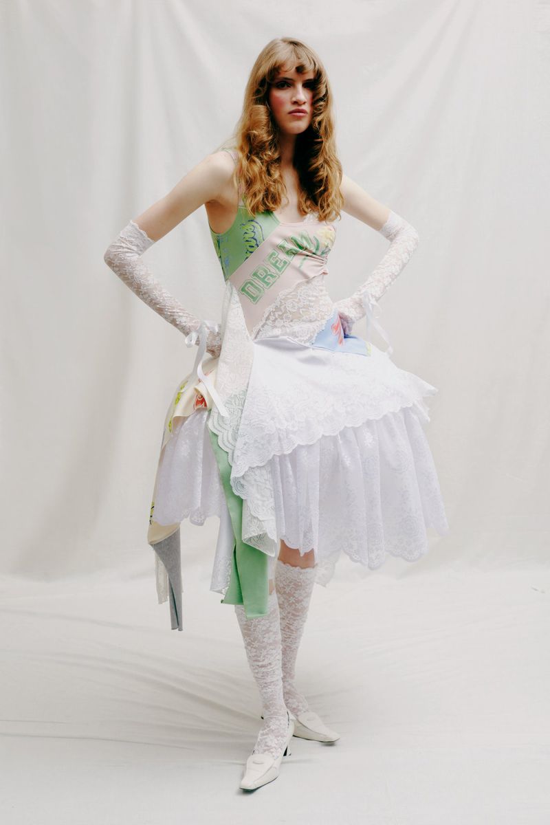 Full-length shot of a model in an asymmetrical dress with lace gloves and stockings, posing in front of a white background.
