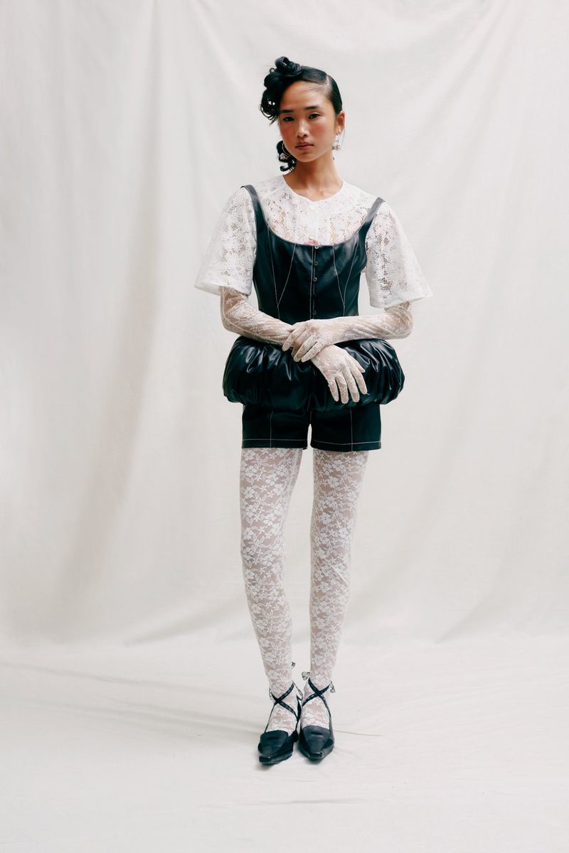 An Asian woman in a fashion pose wearing a black and white outfit consisting of shorts, a lace top and stockings, and cross-strap heels.
