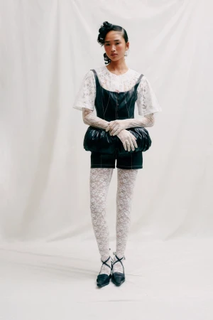 An Asian woman in a fashion pose wearing a black and white outfit consisting of shorts, a lace top and stockings, and cross-strap heels.