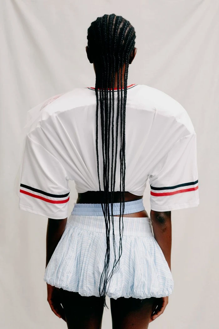 Model seen from behind wearing an oversized white structured top and a pleated skirt against a plain backdrop
