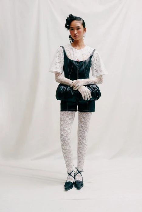 Model in dark leather bustier and shorts over white lace top and tights against white seamless backdrop