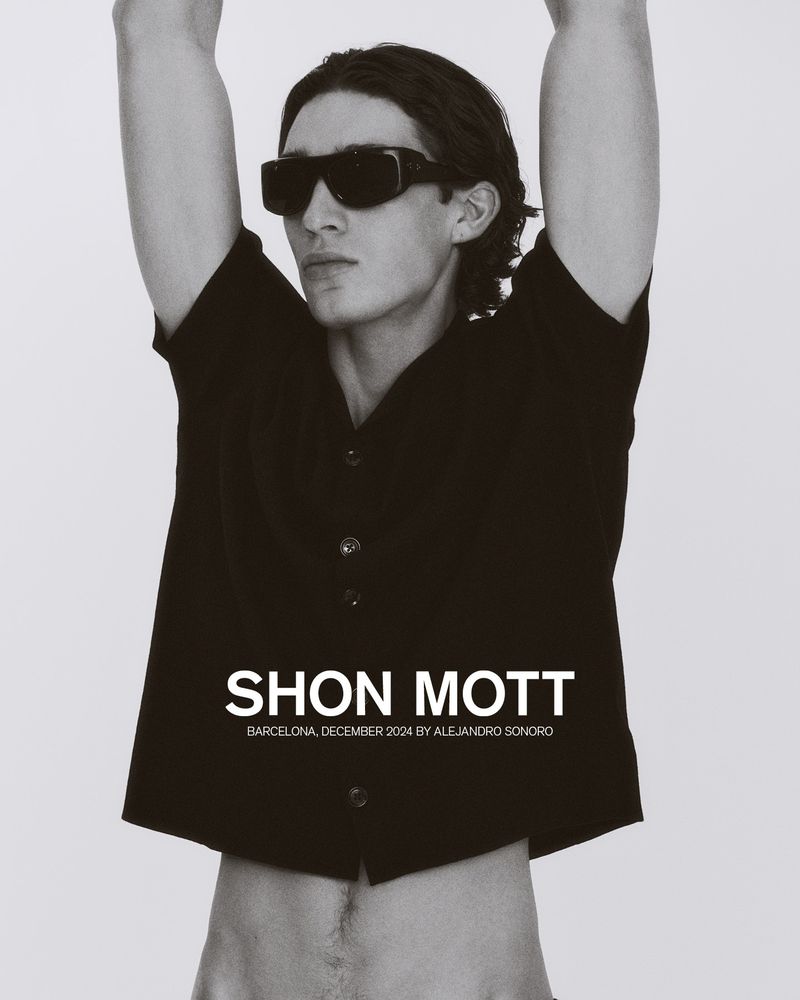 Model in black button-down shirt and sunglasses posing with arms raised against a plain background