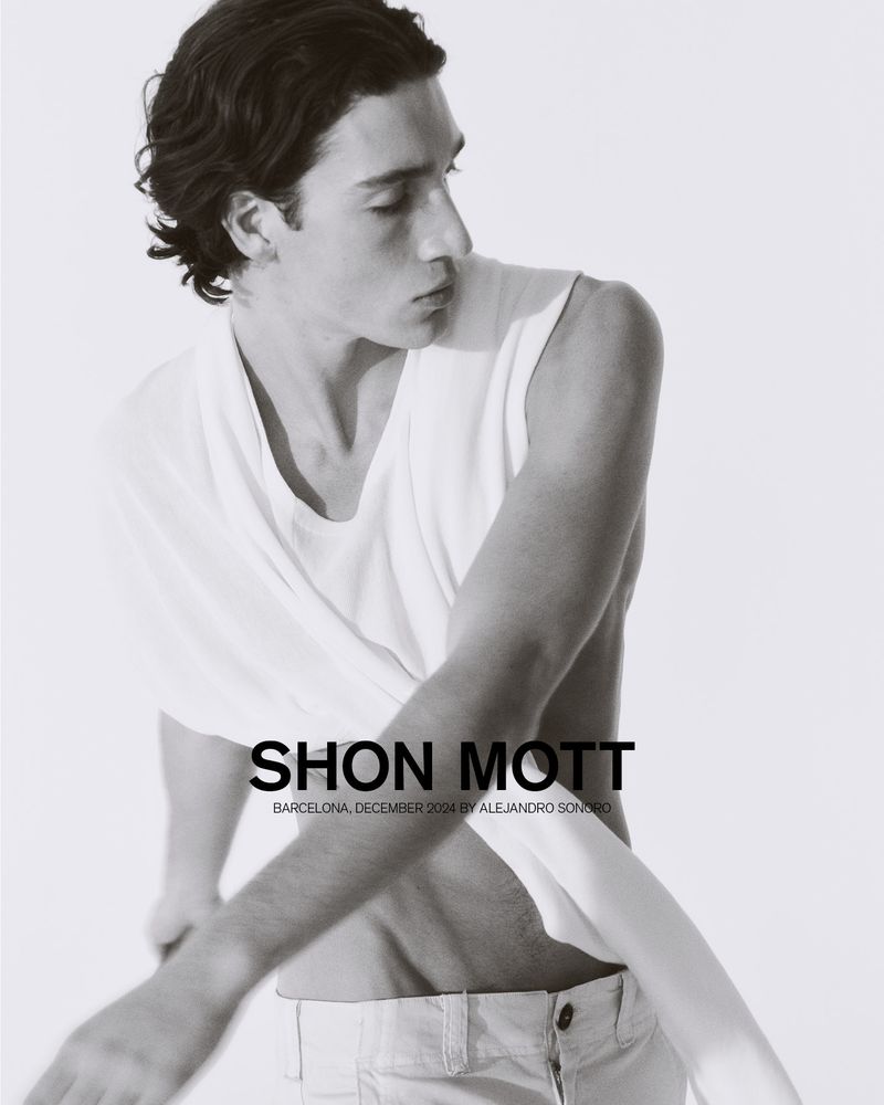 Black and white portrait of a young man in a white top, casually draped, posing in front of a light backdrop with copy overlay.