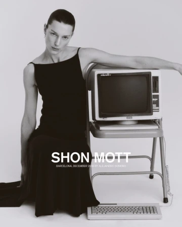 Elegant woman in black dress poses next to vintage computer on grey. Fashion editorial shot; neutral studio backdrop; simple composition.